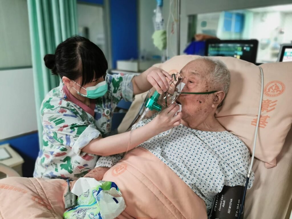 Nurse aids senior patient with oxygen mask in hospital bed, providing care and support.