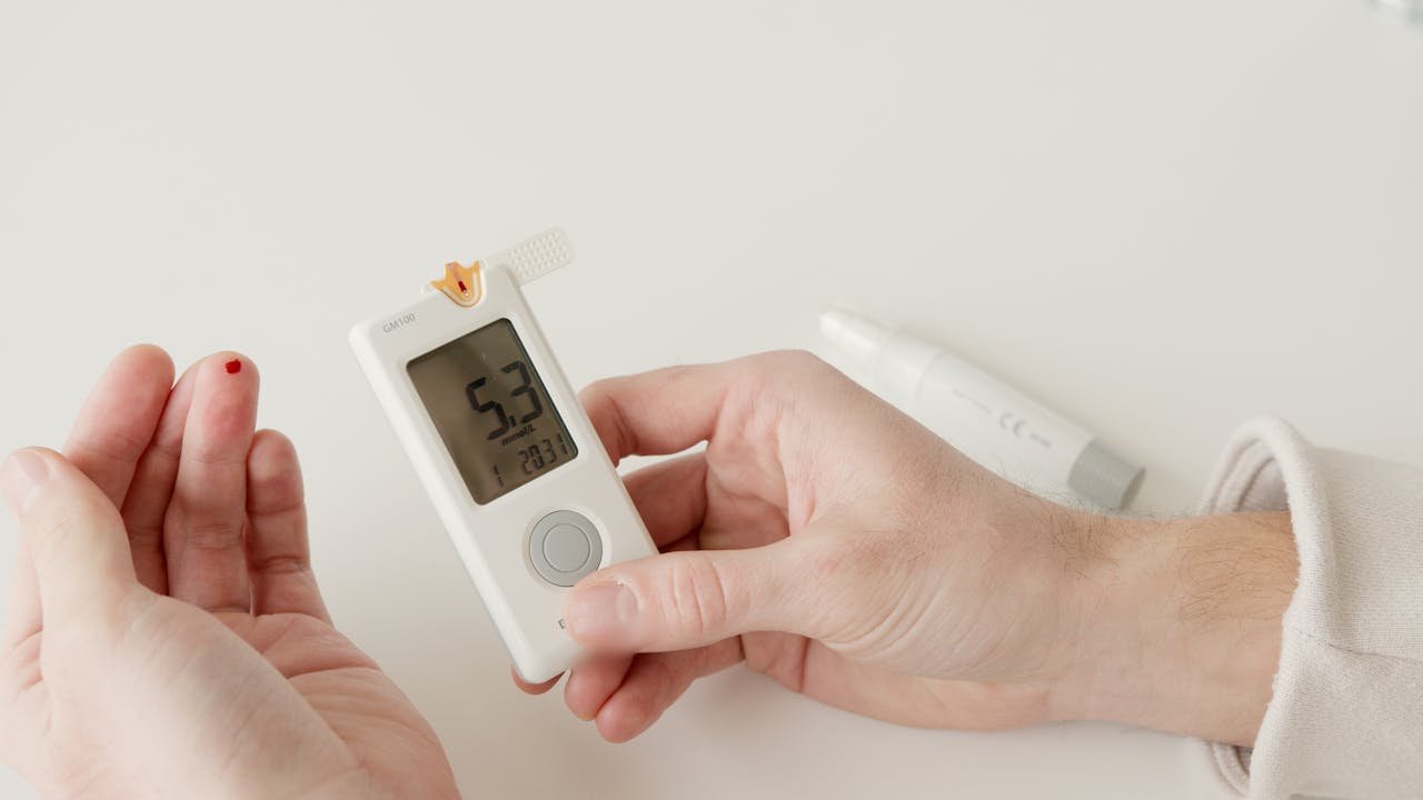 A close-up photo showing a glucometer and a hand pricking to measure blood sugar levels.