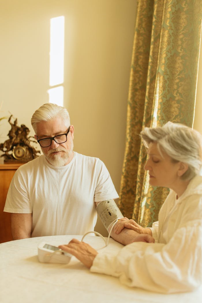 A gray-haired couple using a digital blood pressure monitor in a warmly lit room.